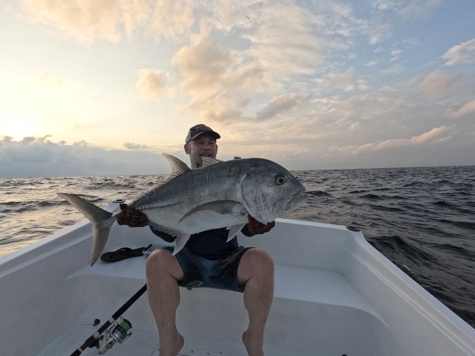 Angler holding a giant trevally on a SALTRIPS boat under a sunset sky