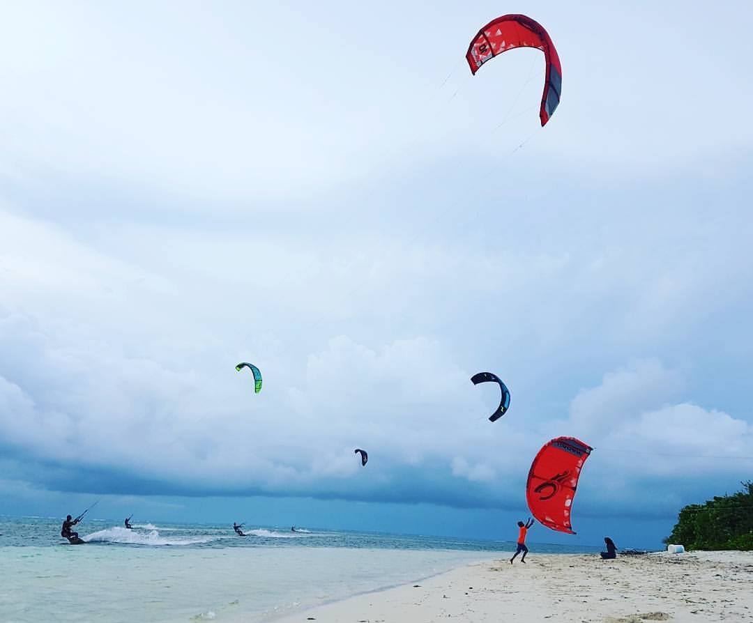 Kiteboarders riding off Goidhoo's white-sand kite beach under a cloudy sky